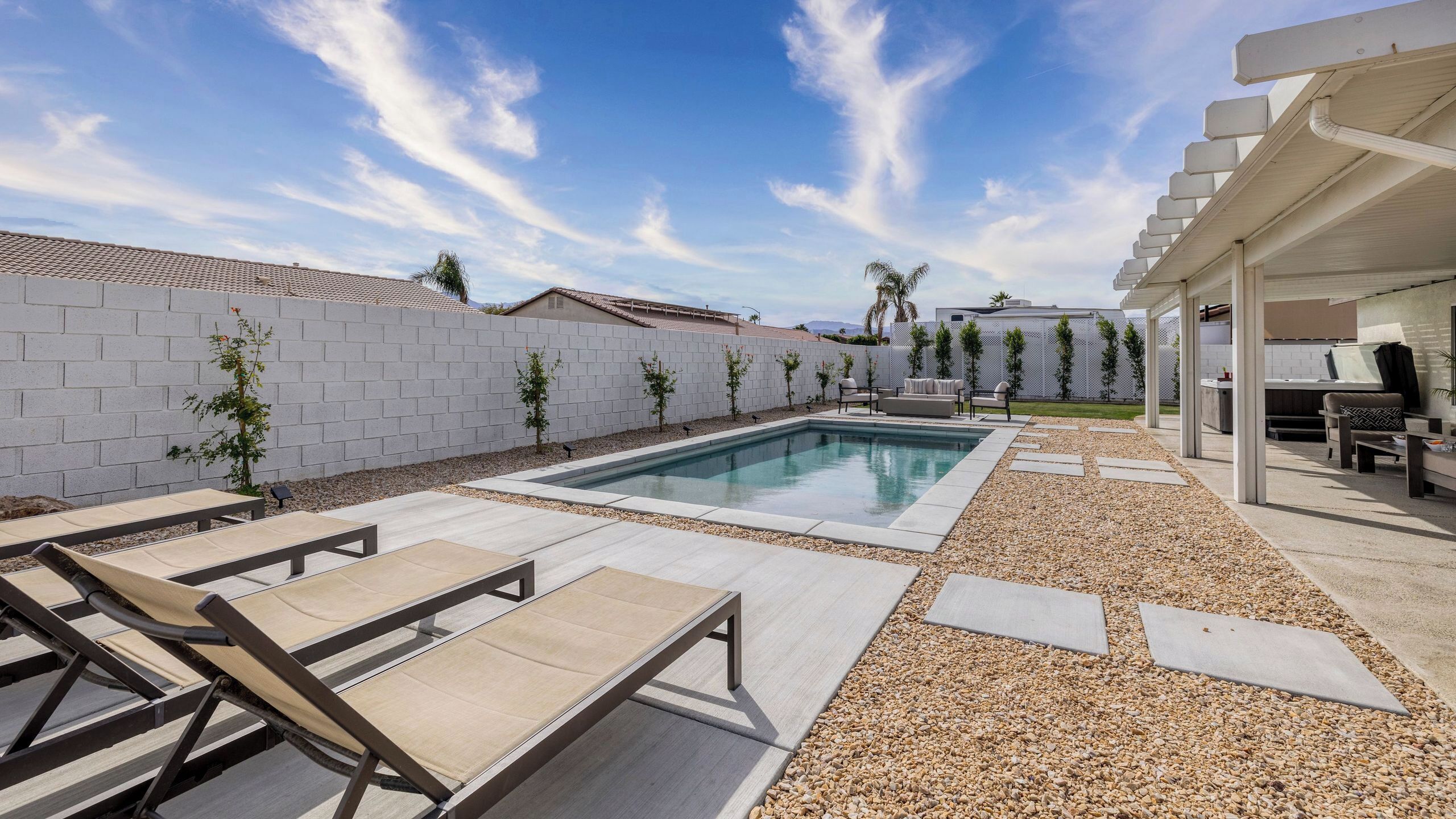 A modern outdoor pool area with lounge chairs, a barbecue area, and a covered patio.