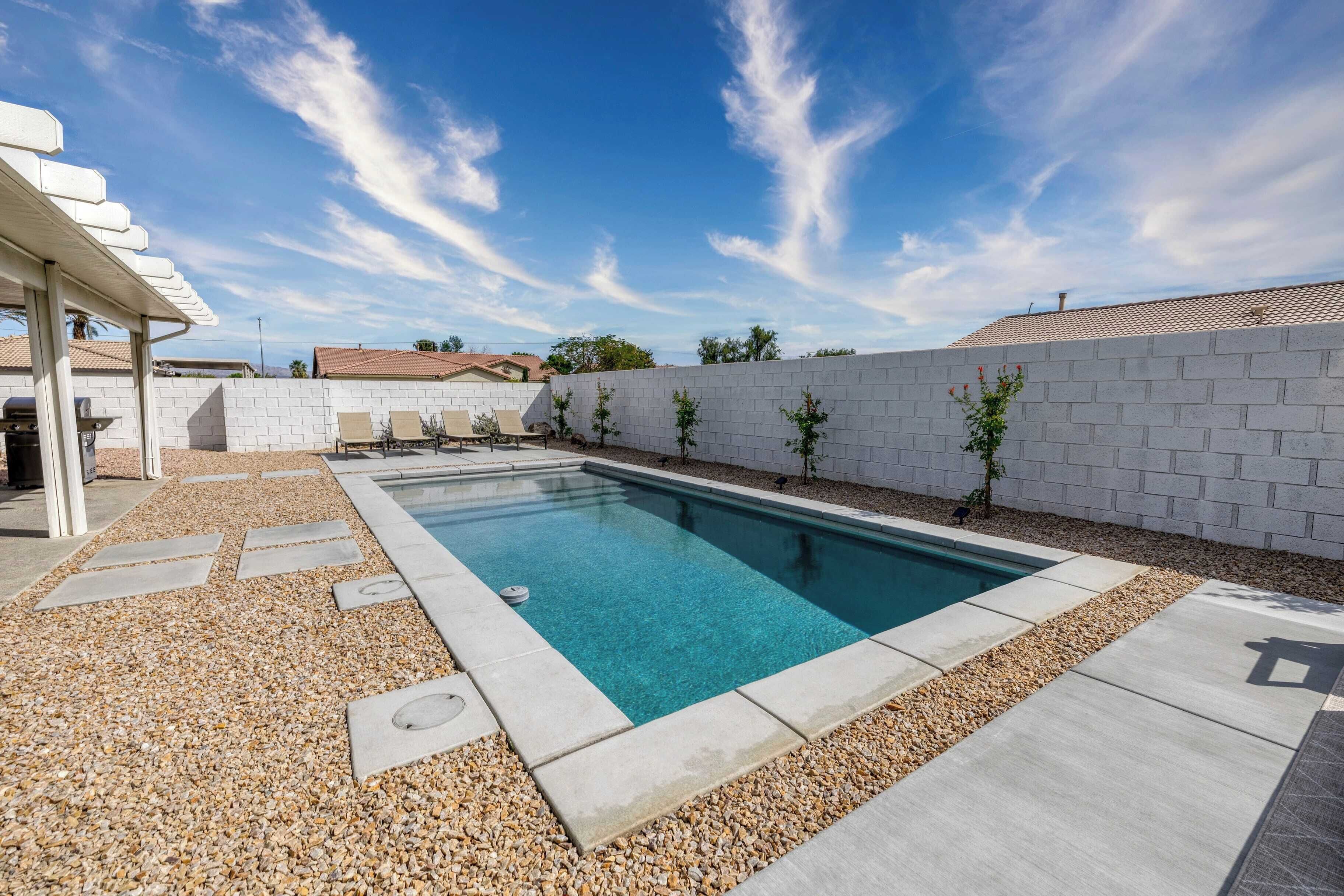 Une piscine rectangulaire à l’eau d’un bleu limpide, entourée d’un mur en briques blanches et d’une zone recouverte de gravier.