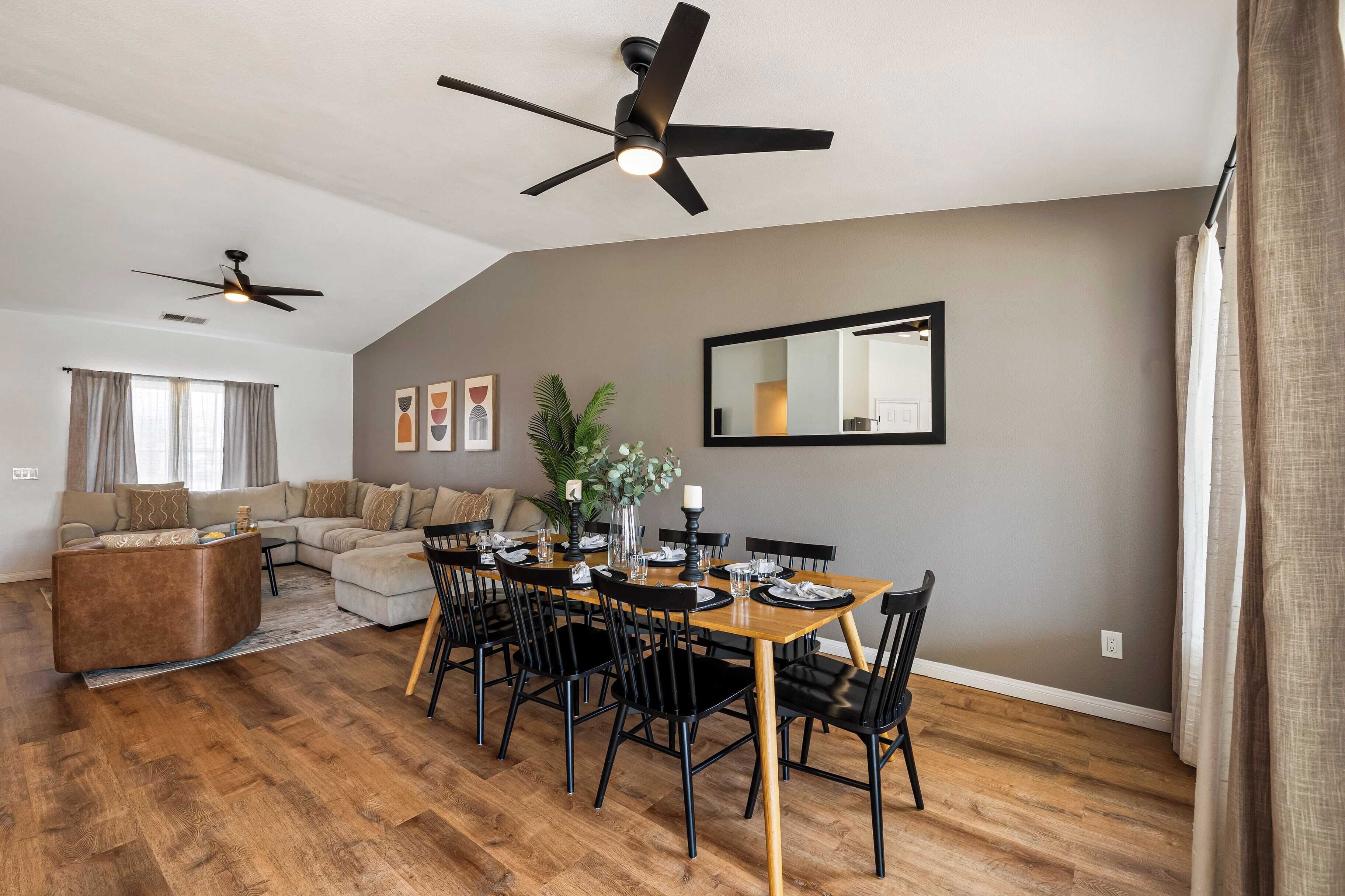 A spacious living area with a dining table set for six, a sofa, and two ceiling fans.