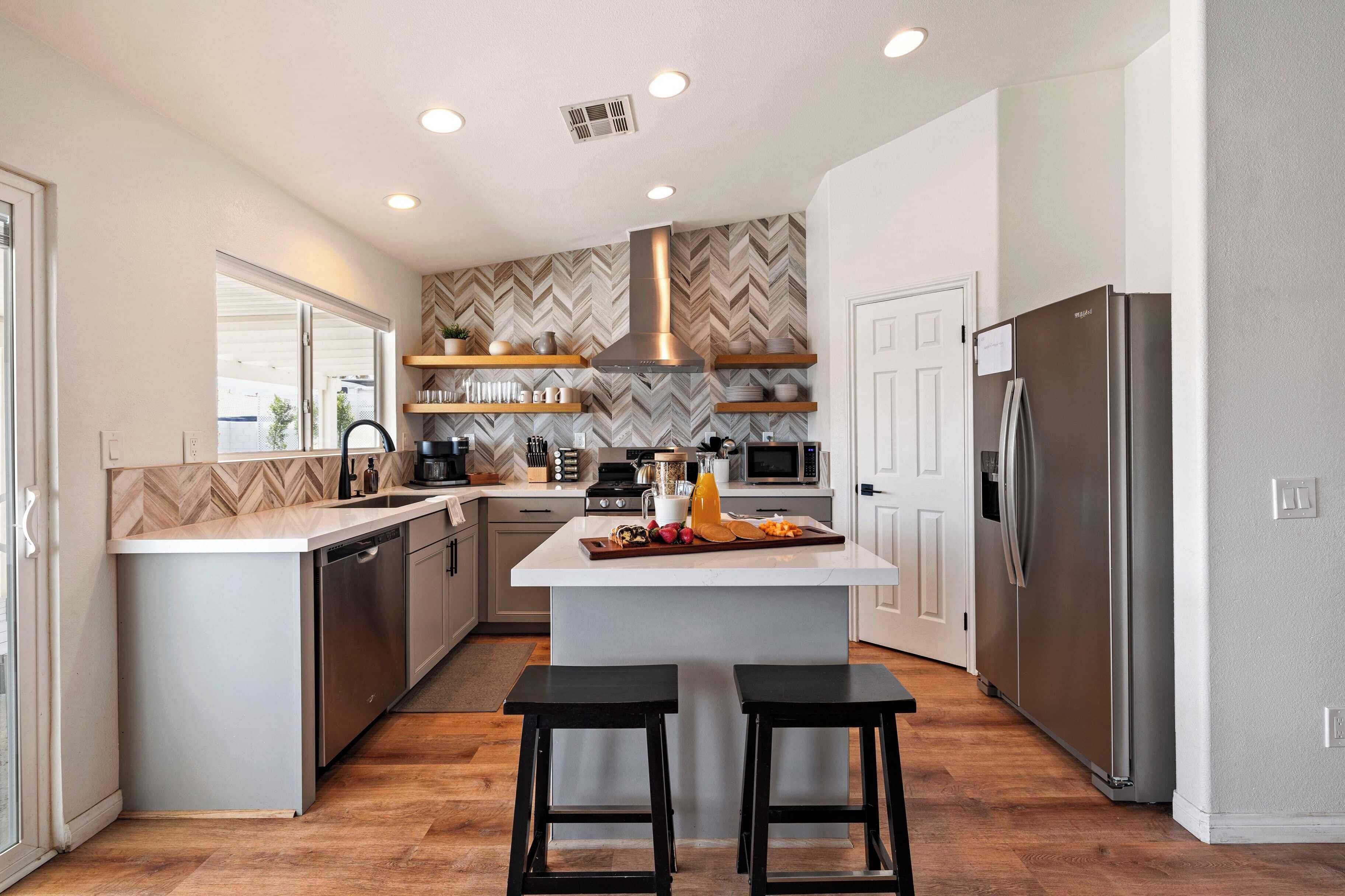 A modern kitchen with a central island, stainless steel appliances, and a herringbone-patterned backsplash.