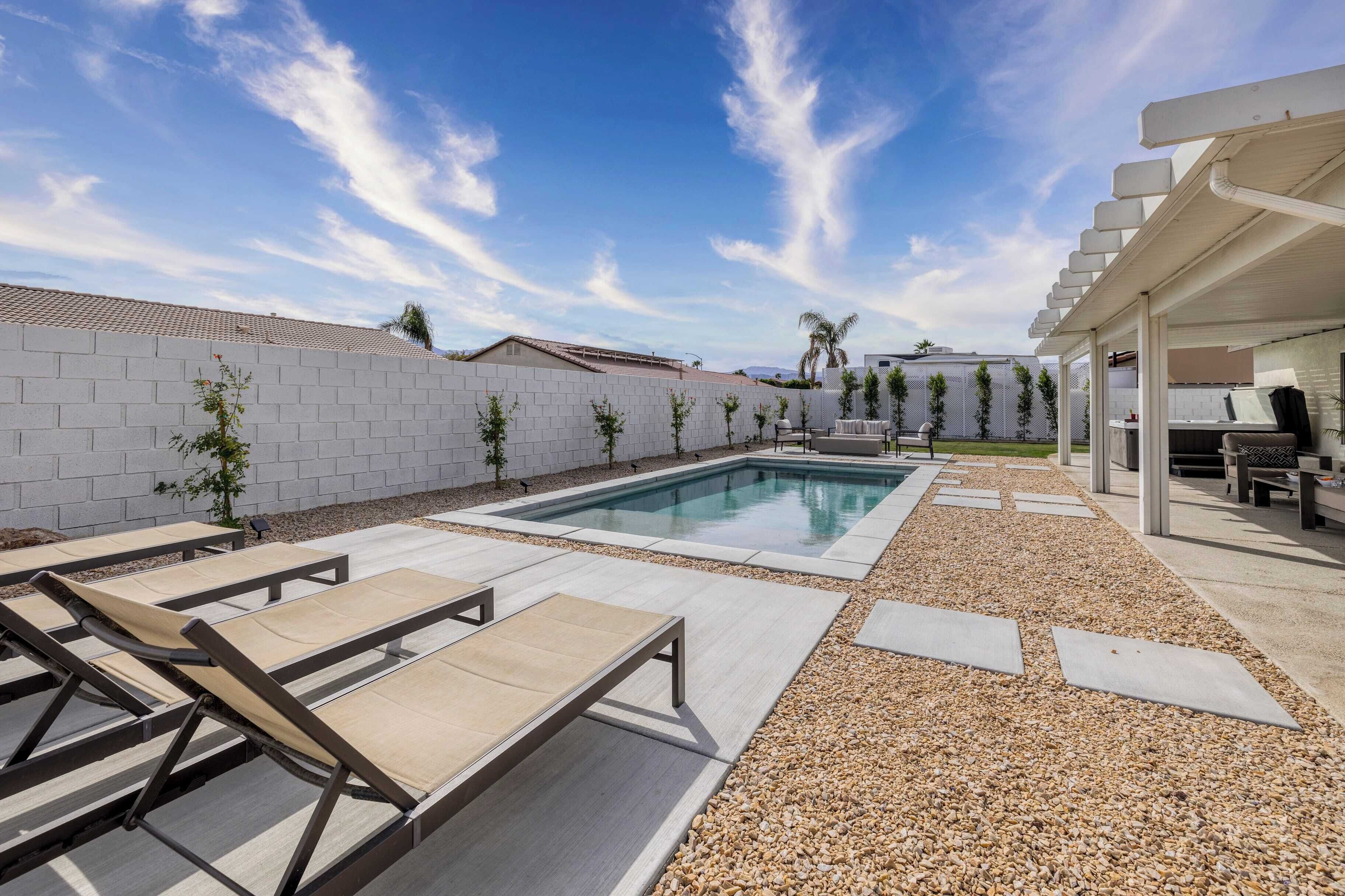 Un espace piscine comprenant des chaises longues, une pergola et une terrasse recouverte de petits galets.
