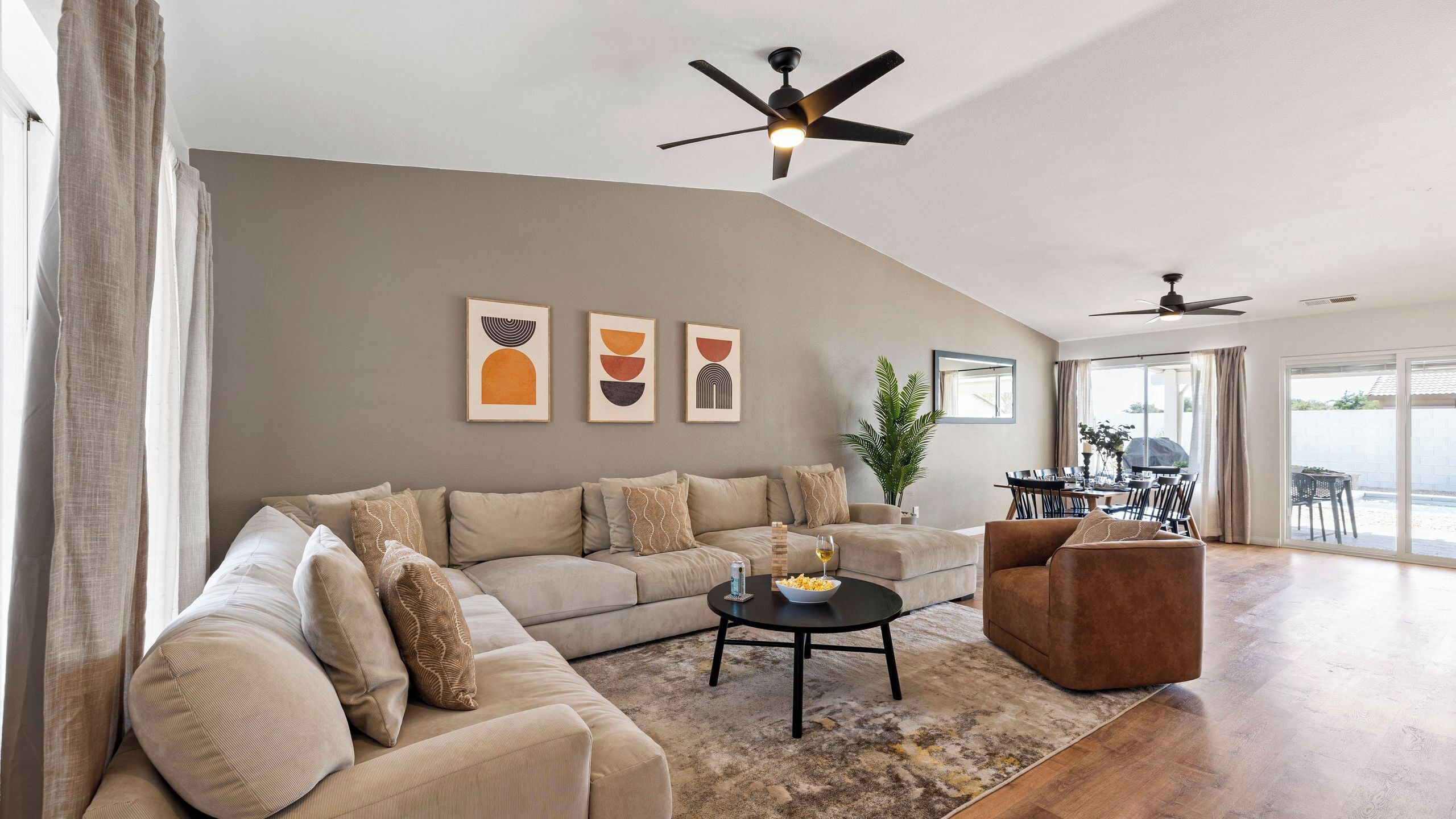 Un salon moderne comprenant un canapé, une table basse et des fauteuils, un coin repas avec une table et des chaises, et un ventilateur de plafond.