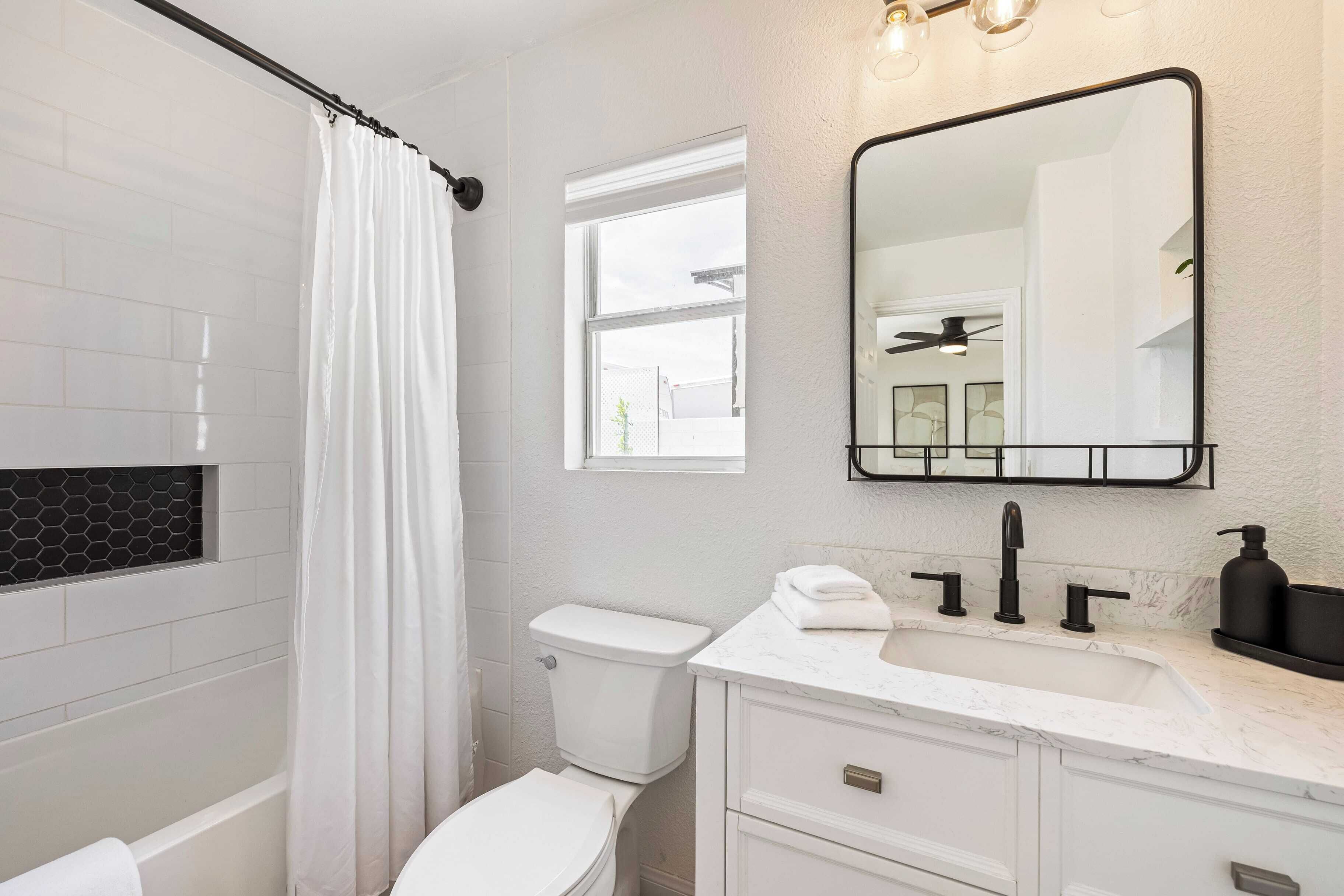 Un baño moderno con inodoro blanco, cortina de ducha, espejo grande y lavabo con encimera de mármol.