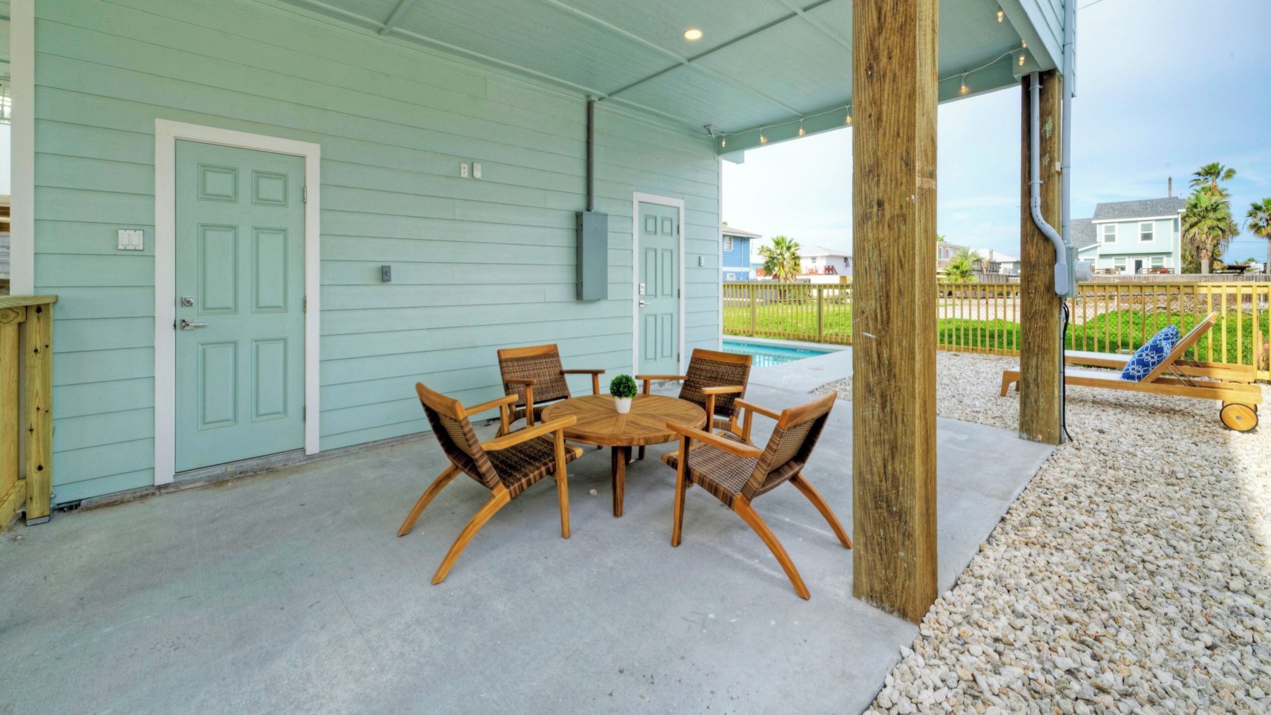 A covered patio with a table and chairs, a pool, and a wooden deck.