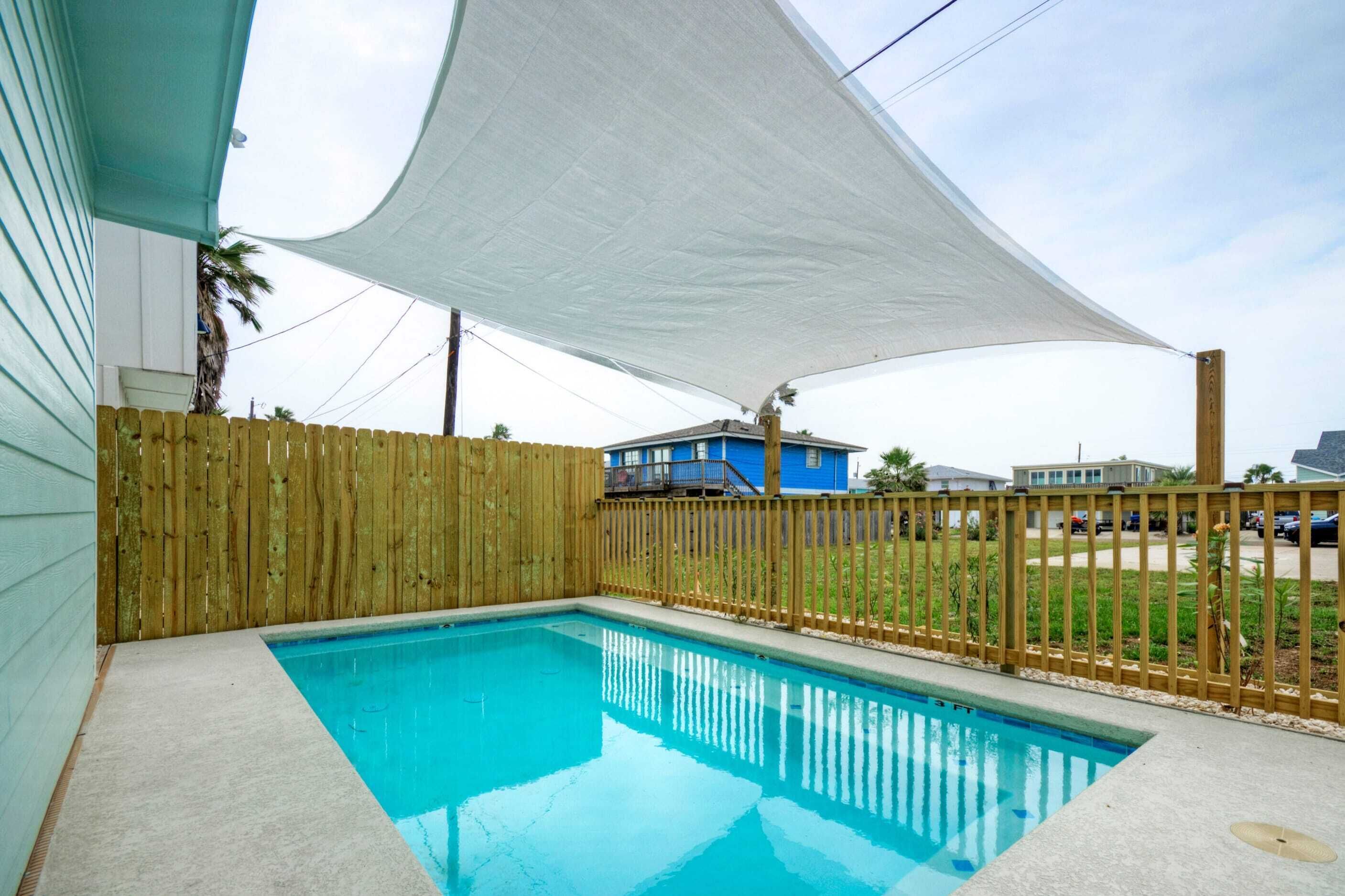 A swimming pool with a wooden fence and a white shade sail.