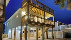 Estructura de madera de dos pisos con balcones, elevada sobre pilotes y rodeada por una valla blanca.