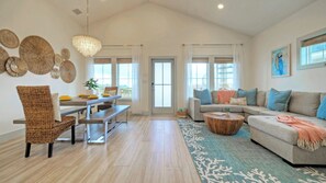 A spacious living room with a high ceiling, a dining area with a bench, and a sofa with cushions. - Casa Rita by Avantstay Snowbird Discounted Rates Private Pool, Near Beach (Port Aransas)