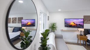 Quarto moderno com um espelho grande, duas mesas de cabeceira, um sofá e uma televisão.