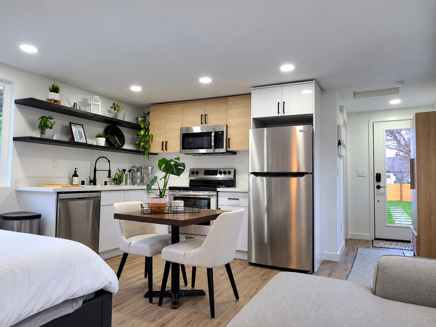 A modern kitchen with a dining area, stainless steel appliances, and a view of the outdoors.