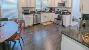 A modern kitchen with white cabinets, stainless steel appliances, and a dining area with a round table and chairs. - Newly Renovated, Charming Home Near Downtown! (Chattanooga)