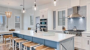Una cocina moderna con una isla grande, armarios blancos y una campana de acero inoxidable.