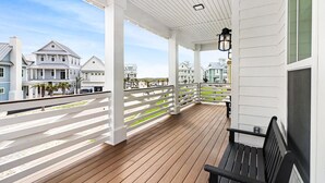 Een overdekt houten terras met een witte balustrade, een bank en een hangende lamp.