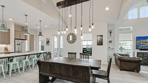 Een ruime keuken met een centraal eiland, hangende verlichting en een grote klok aan de muur.