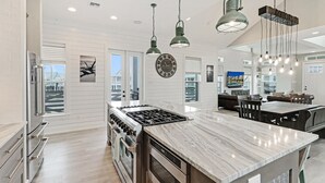 Een moderne keuken met een centraal eiland, roestvrijstalen apparatuur en hangende lampen.