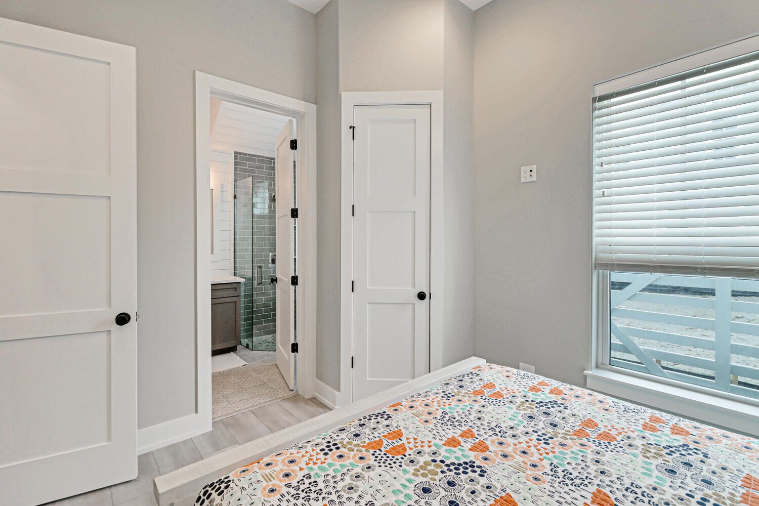 A bedroom with a bed, a window with blinds, and a door leading to a bathroom.