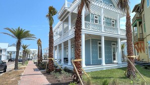 A two-story house with a balcony, surrounded by palm trees and a brick pathway. - Emergensea 200 LAU (Port Aransas)