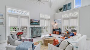 A spacious living room with a high ceiling, large windows, a fireplace, and a view of the outside. - Emergensea 200 LAU (Port Aransas)