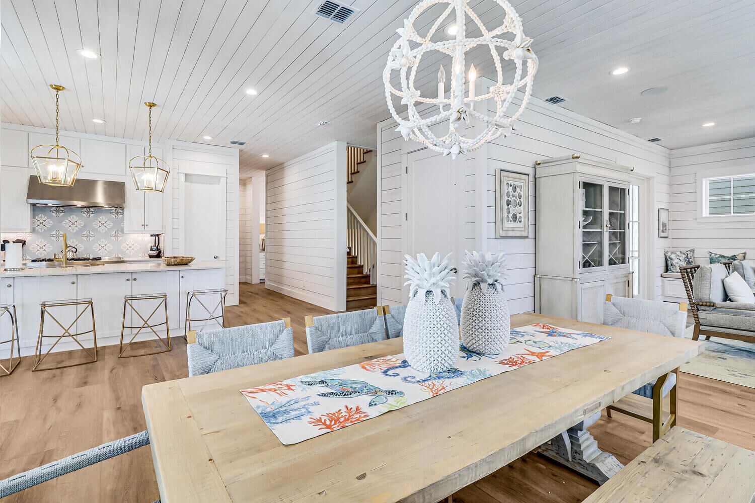 A spacious dining area with a wooden table, blue and orange patterned table runner, and decorative pineapples.