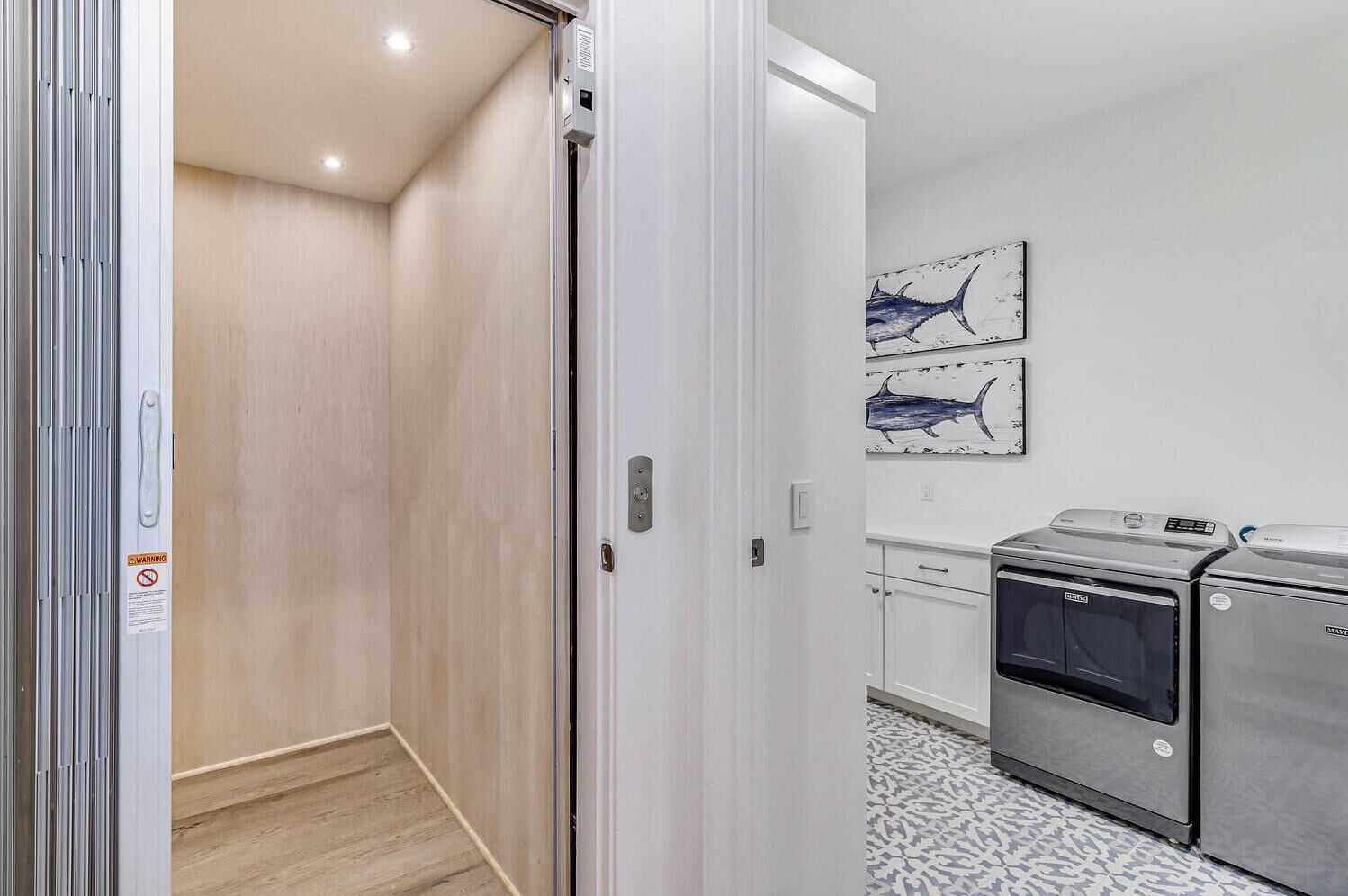A modern kitchen with stainless steel appliances, a wooden floor, and a wall-mounted artwork of fish.