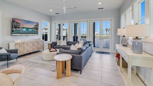 A spacious living room with a gray sofa, a coffee table, and a TV mounted on the wall. - Surf Camp 104 NEI (Port Aransas)