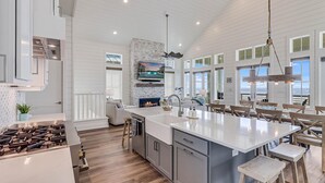 A modern kitchen with a large island, a fireplace, and a view of the ocean. - Livin' the Dream 136 TUC (Port Aransas)