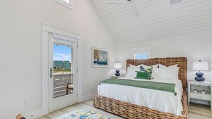 A bedroom with a large bed, a wicker headboard, a white door leading to a balcony, and a small bedside table with a lamp. - Rose All Day 220 Esc-c (Port Aransas)