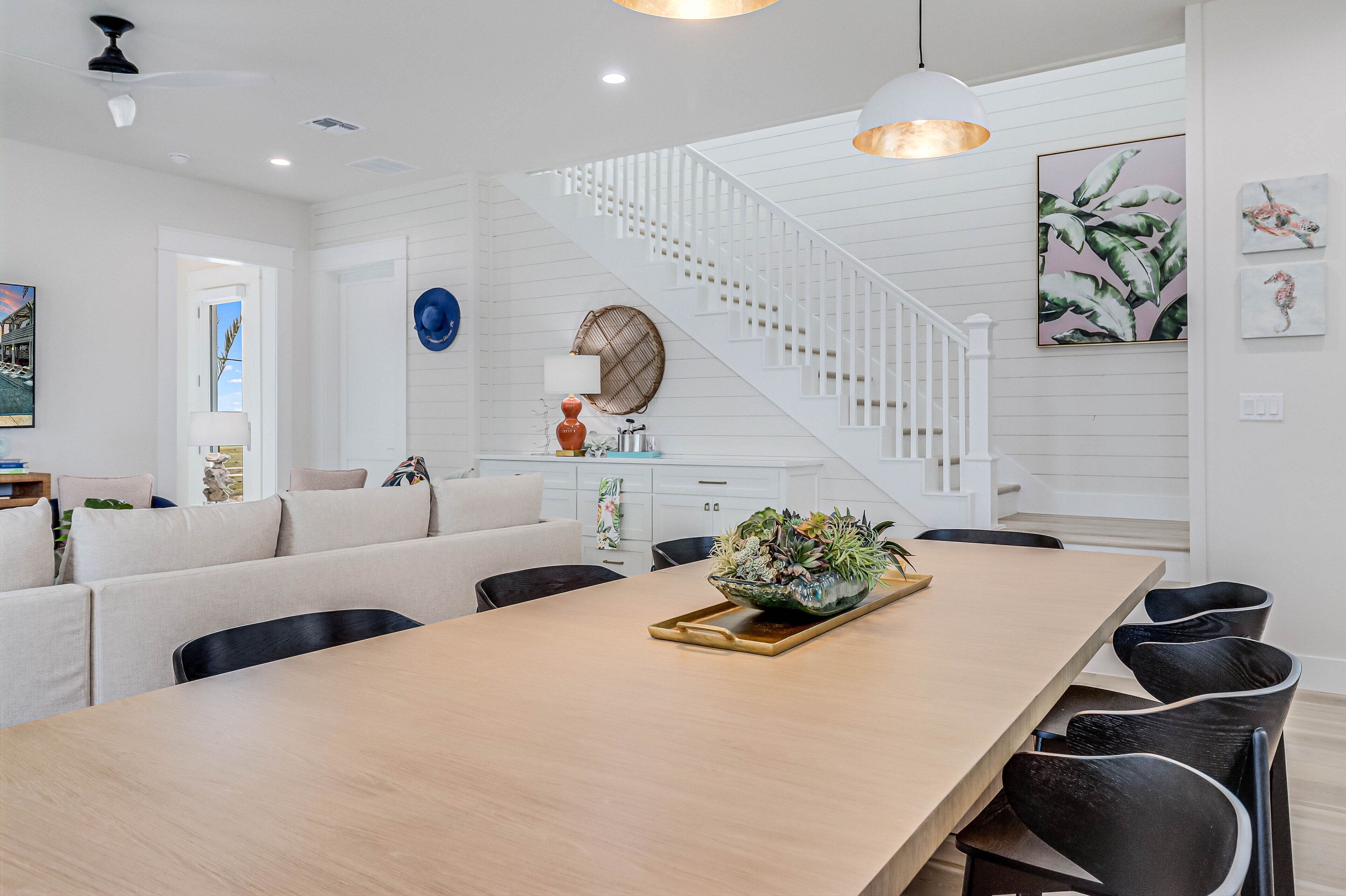 A modern kitchen with a wooden table, black chairs, and a staircase with white railings.