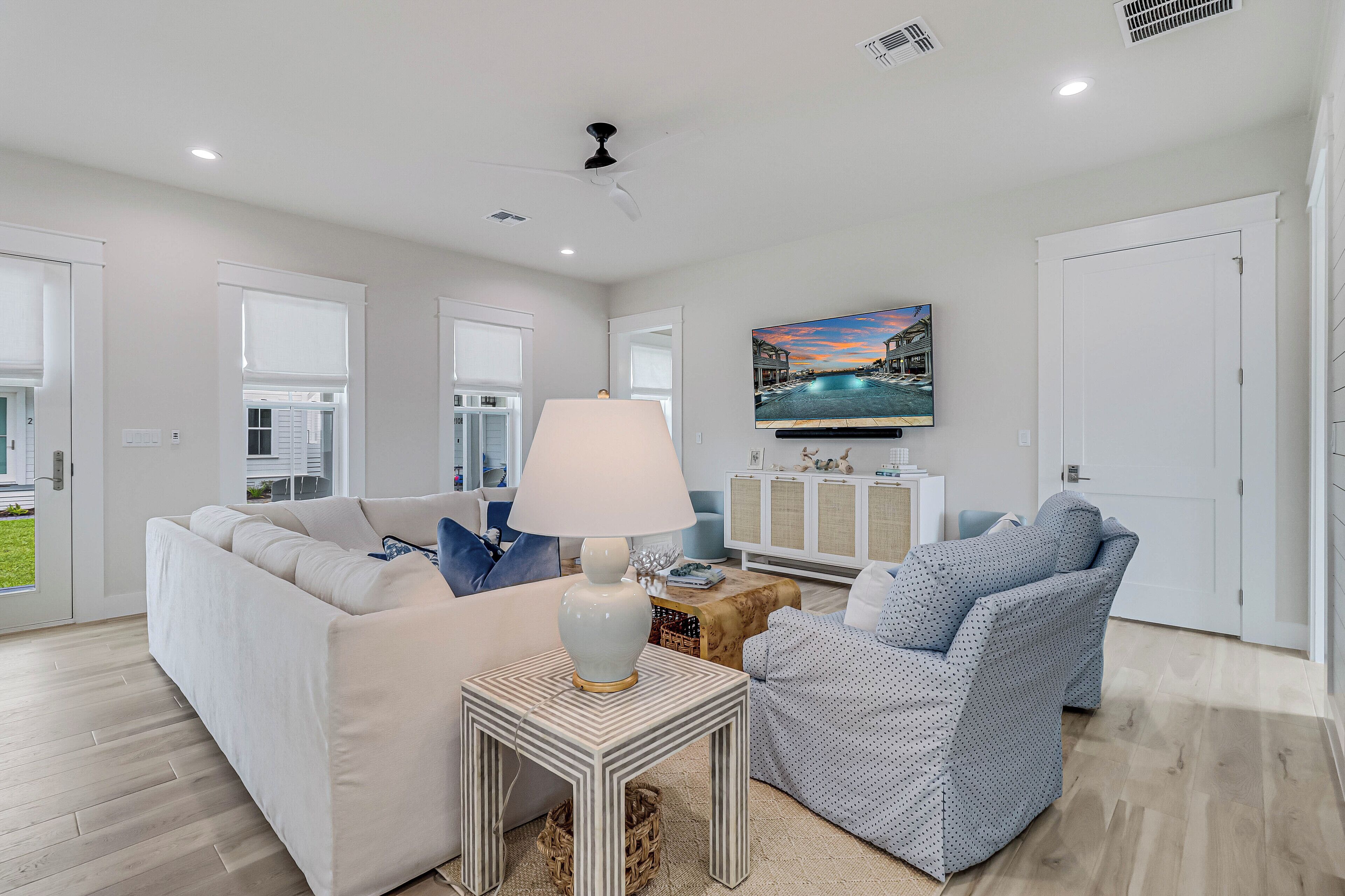 A modern living room with a white sofa, a patterned armchair, a small side table with a lamp, and a television mounted on the wall.