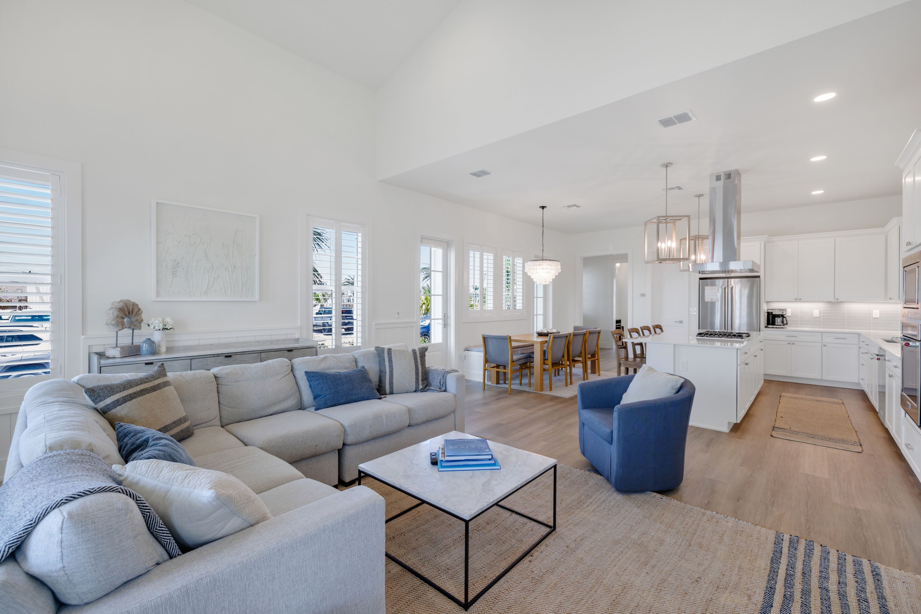 A spacious living area with a sofa, coffee table, and dining area with chairs and a kitchen in the background.