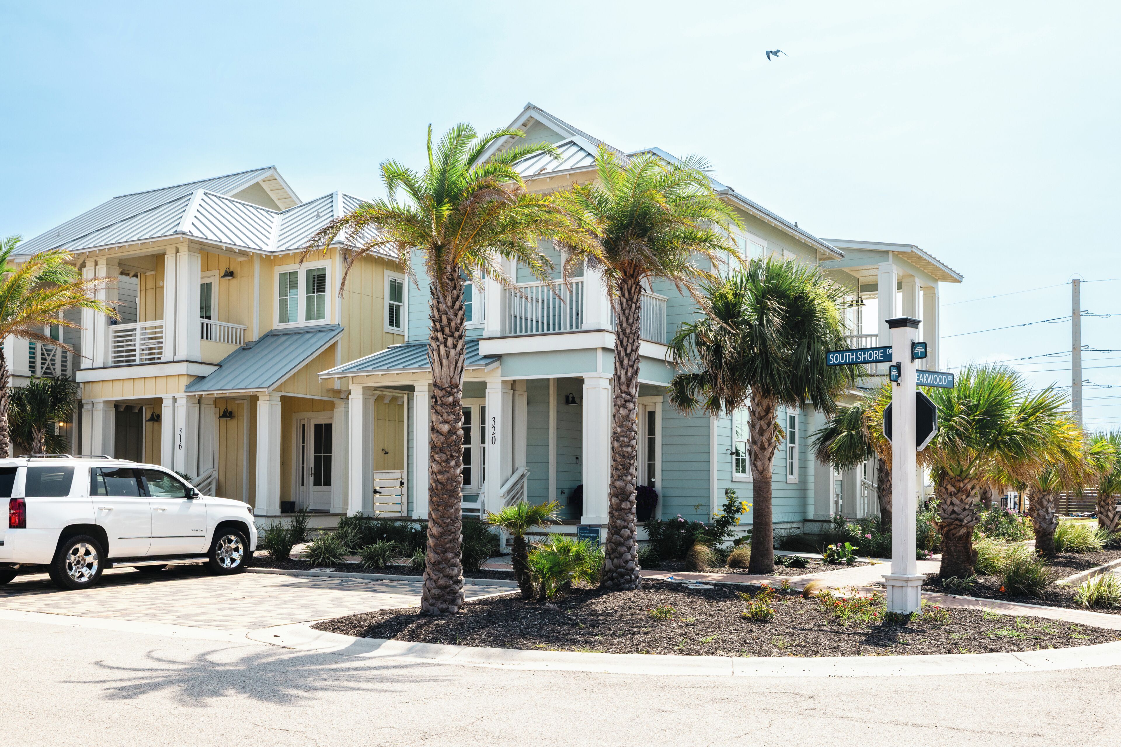 A two-story house with a balcony, palm trees, and a street sign.