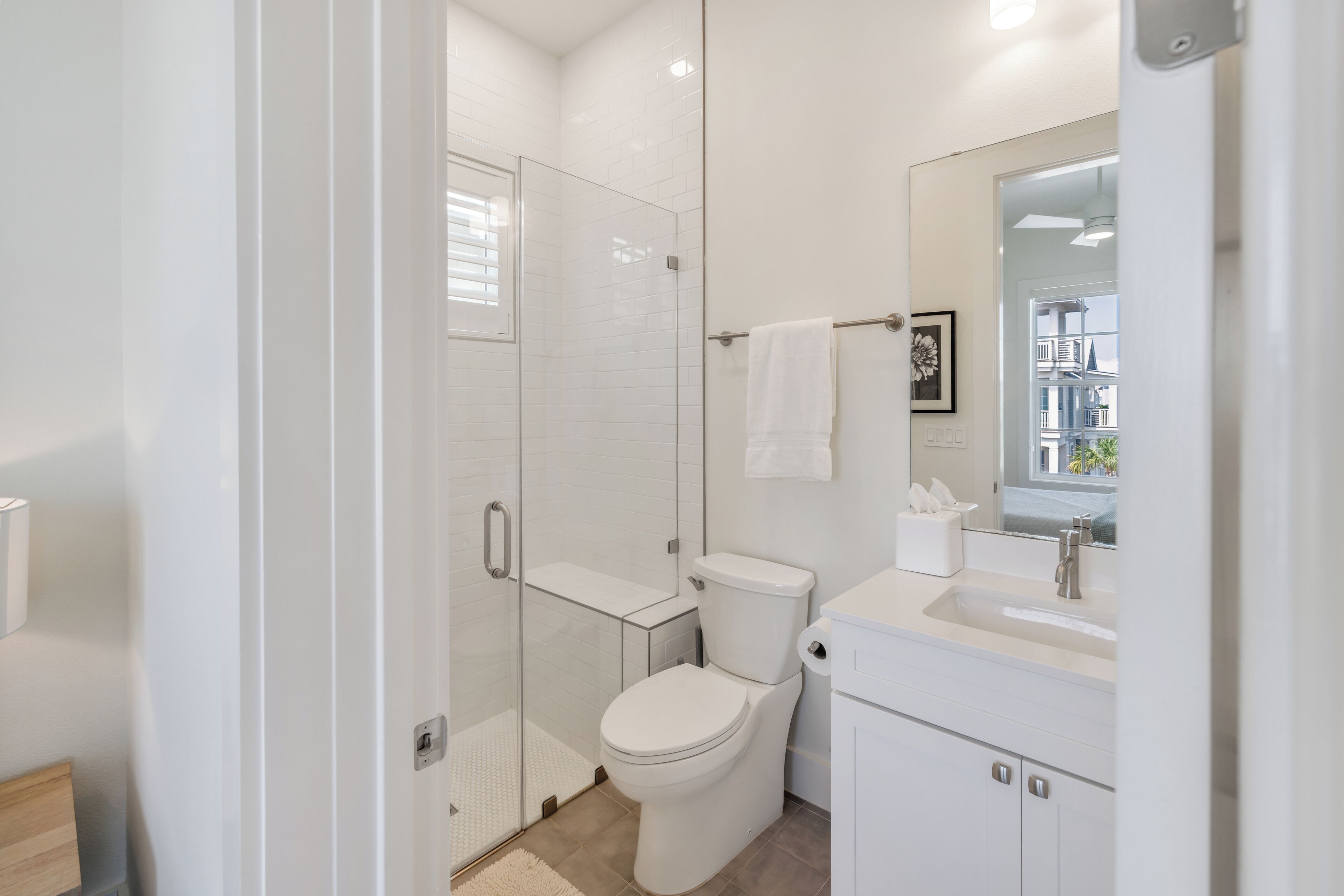 Une salle de bain moderne avec une douche à parois de verre, des toilettes blanches et un lavabo surmonté d’un miroir.