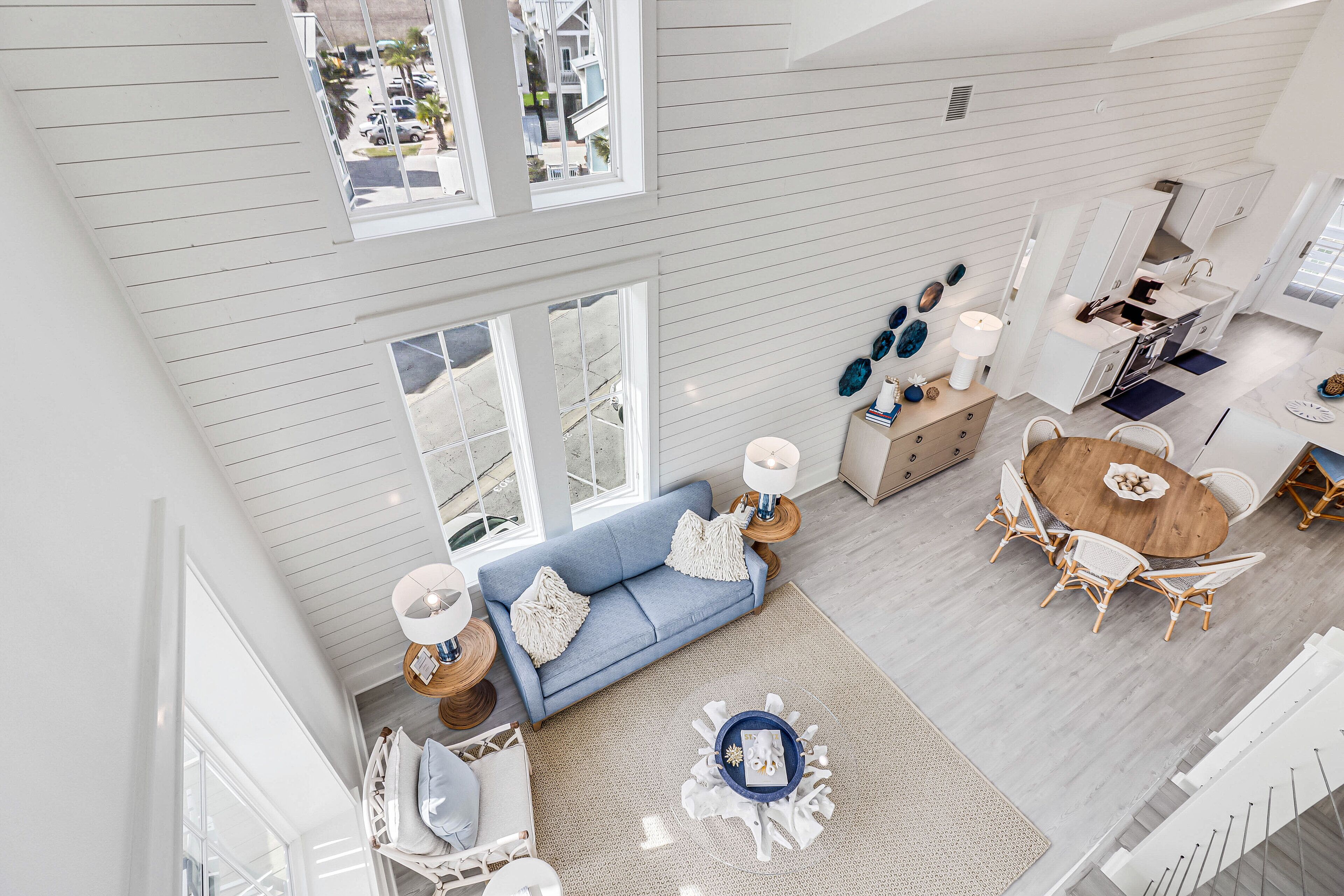 A spacious living area with a blue sofa, dining table, and chairs, a kitchen area, and large windows offering a view of the street.