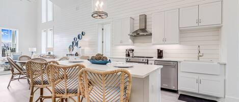 Une cuisine moderne avec des meubles blancs, un îlot central, des chaises en osier et un ventilateur de plafond.
