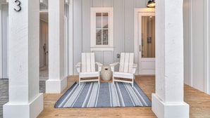 A hallway with white painted columns, a blue striped rug, two white Adirondack chairs, and a small decorative vase. - Casa Del Sol 213 TEA (Port Aransas)