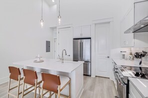 A modern kitchen with white cabinetry, a stainless steel refrigerator, a built-in oven, and a large island with bar stools.
