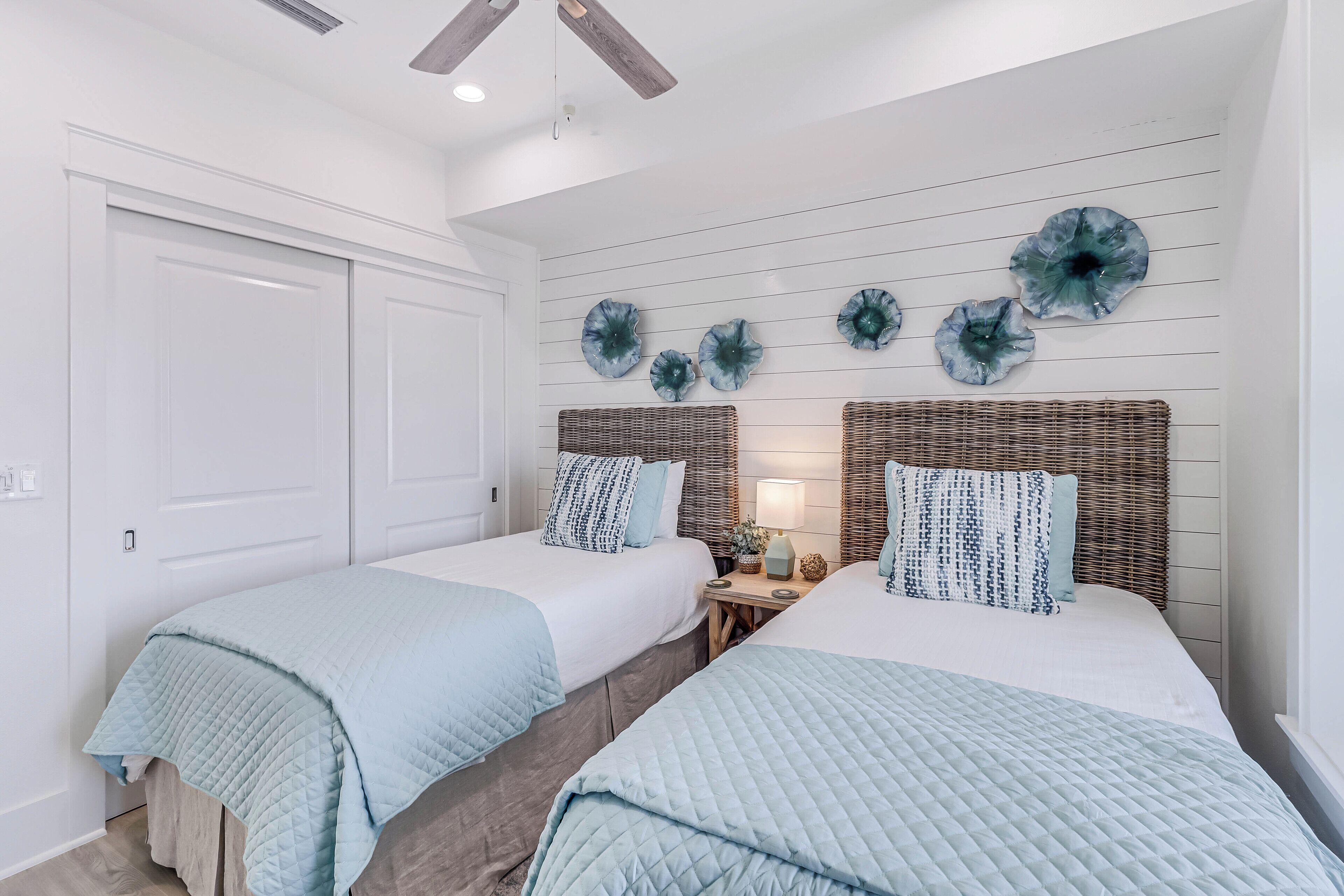Une chambre avec deux lits, un ventilateur de plafond et des œuvres d’art décoratives au mur.