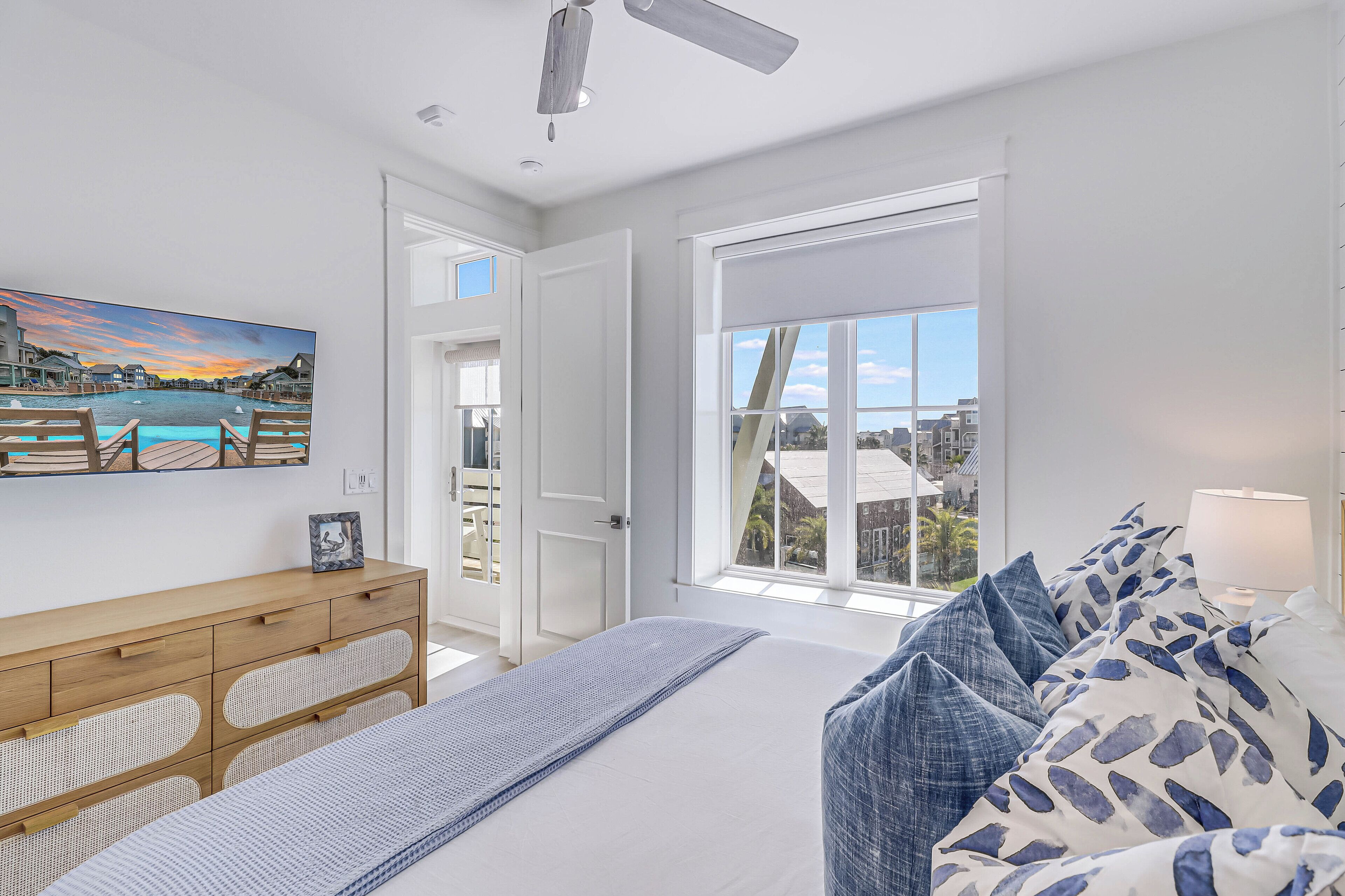 A bedroom with a large bed, a wooden dresser, a bench, and a view of the city through a large window.
