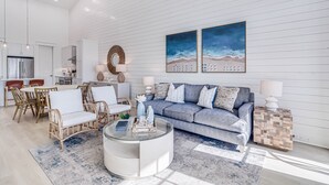Un salon moderne avec un canapé bleu, des fauteuils en osier, une table basse en verre et des œuvres d’art accrochées au mur.