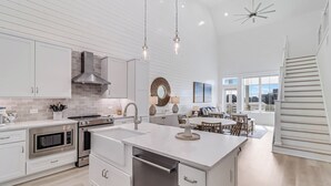 Une cuisine moderne avec des meubles blancs, des appareils en acier inoxydable et des luminaires suspendus.