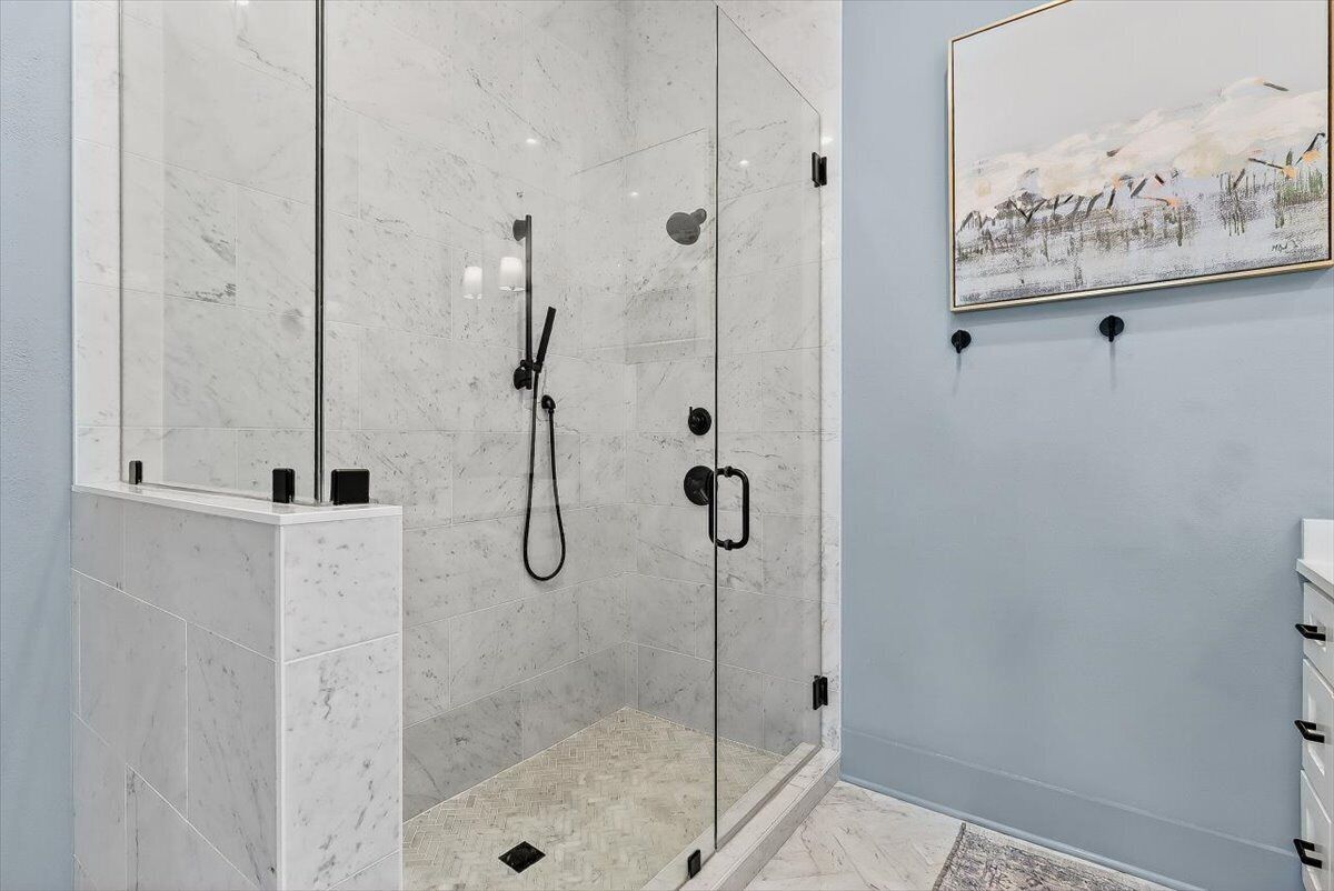 A modern bathroom with a glass-enclosed shower, marble tiles, and a painting on the wall.