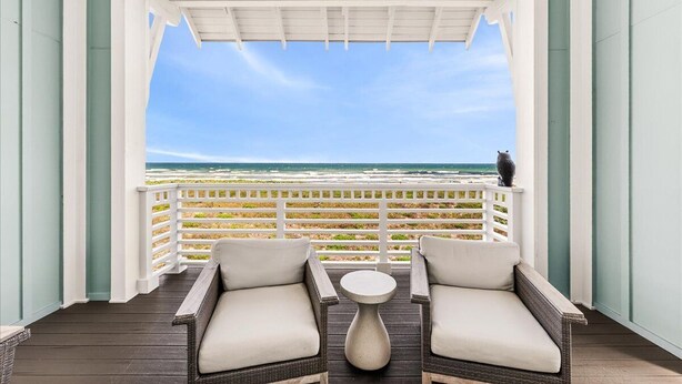 A balcony with wicker furniture, a small table, and a view of the ocean. - Blue Havana 104 DAR (Port Aransas)