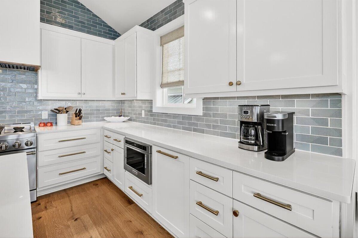 A modern kitchen with white cabinets, a built-in oven, a coffee maker, and a window with a view.