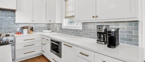 A modern kitchen with white cabinets, a built-in oven, a coffee maker, and a window with a view.