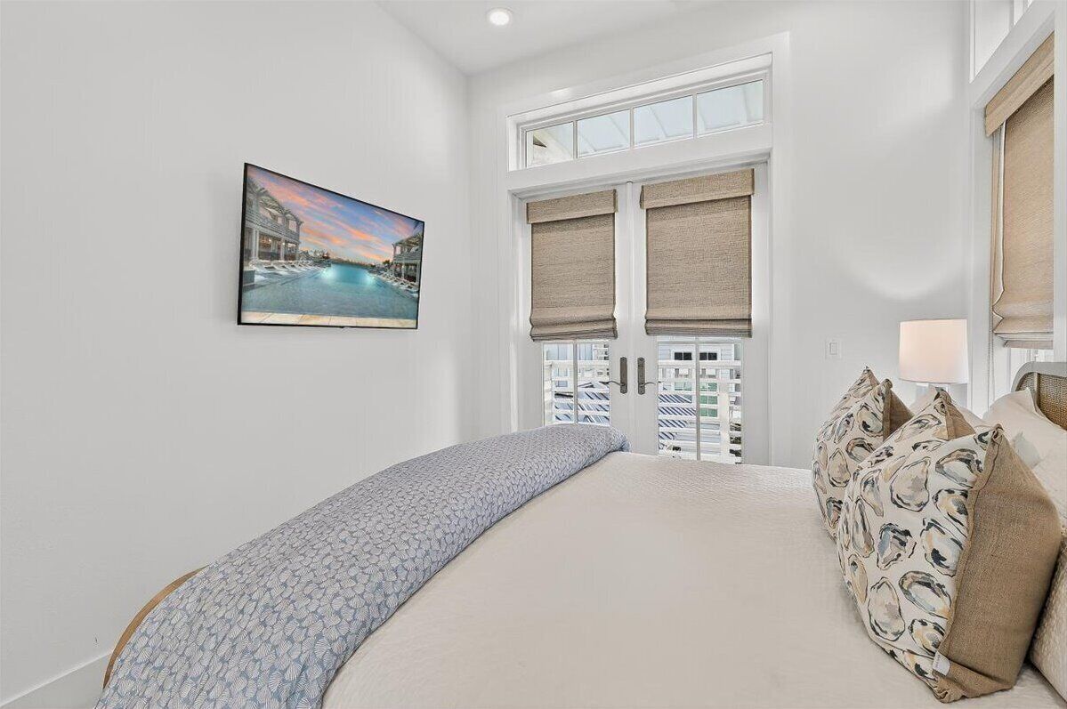A bedroom with a bed, a painting of a beach scene, and a window with blinds.