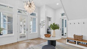 A spacious living room with a large window, a round table, and a bench. - Blue Havana 104 DAR (Port Aransas)