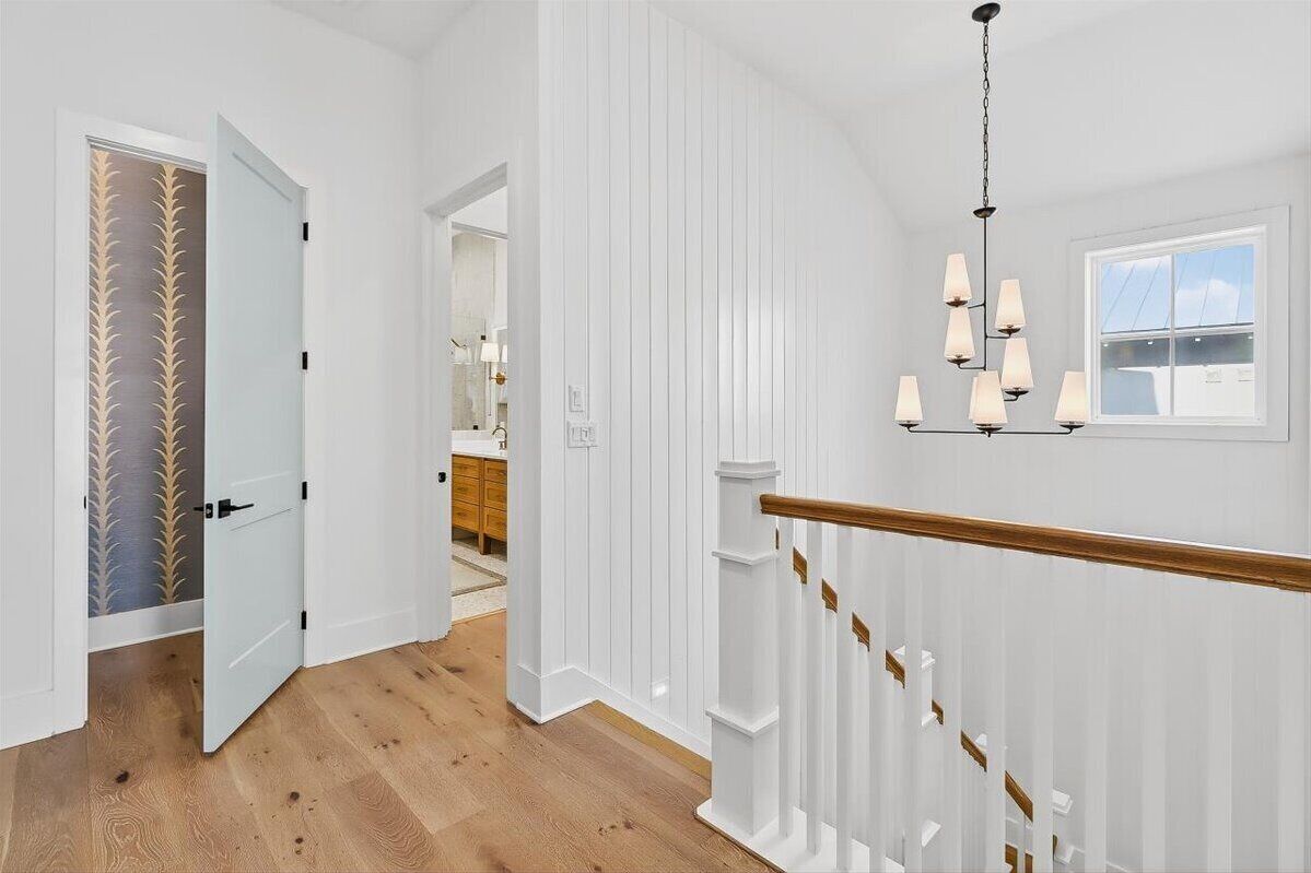 Un pasillo con paredes blancas, suelo de madera y una escalera con barandilla blanca.