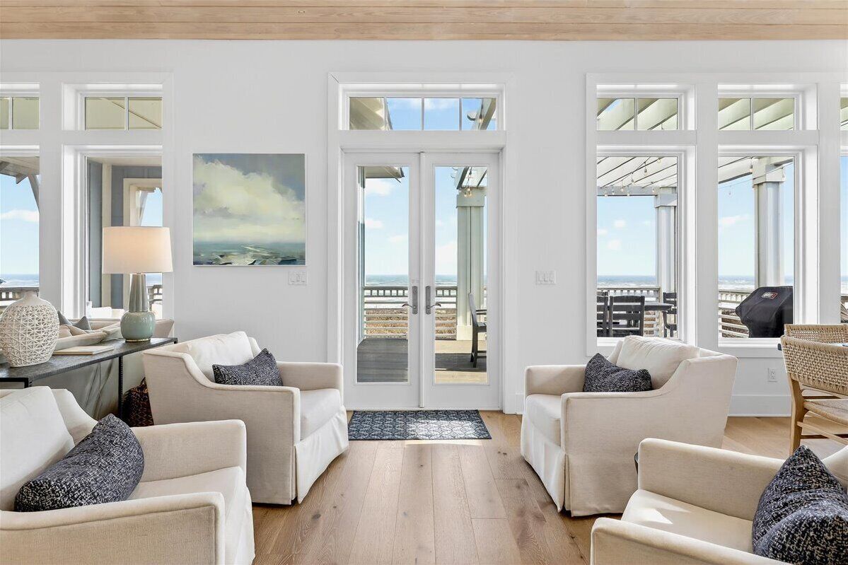 Een ruime woonkamer met witte meubels, een groot raam en uitzicht op de oceaan.