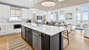 A modern kitchen with a large island, stainless steel appliances, and a view to the outside. - Blue Havana 104 DAR (Port Aransas)