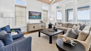 A spacious living room with a large sofa set, a coffee table, and a view of the ocean through large windows. - Blue Havana 104 DAR (Port Aransas)