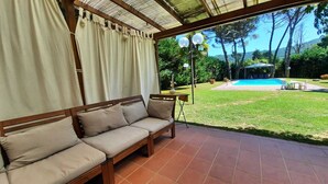 A covered patio with a wooden sofa, a small table, and a view of a swimming pool and garden. - Super Villa met 5 Slaapkamers, max 10 Pers, Groot Privé Zwembad & Heerlijke Tuin (Monsagrati)